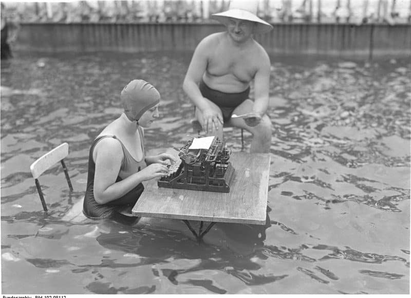 Altes Schwarz-Weiss Foto: Sekretärin mit Schreibmaschine und Chef sitzen im Wasser, um der Hitze zu entgehen.