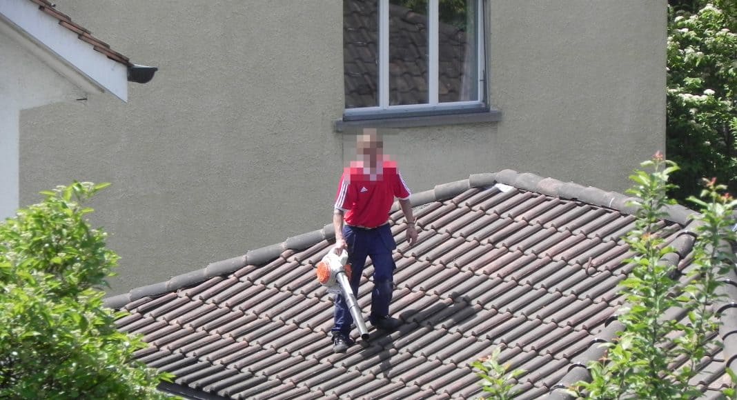 Mann steht mit Laubbläser auf seinem Hausdach.